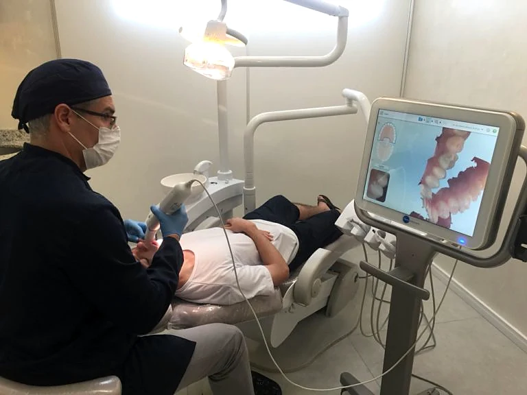 Escaneamento intraoral sendo realizado em uma paciente, com a imagem 3D na tela